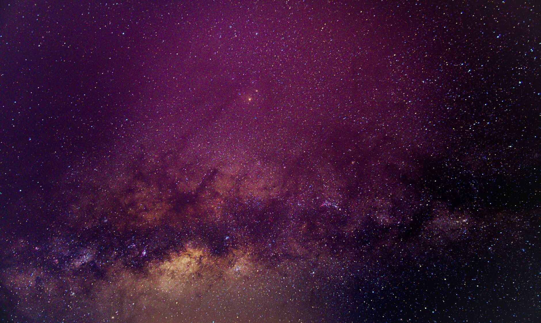 The Milky Way with a warm golden core arcing across a deep purple night sky